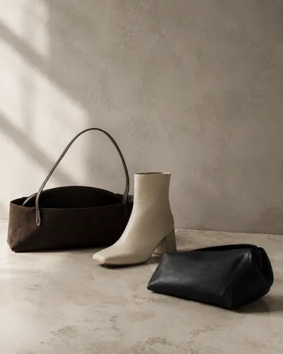 A brown suede bag and a black clutch beside a cream ankle boot